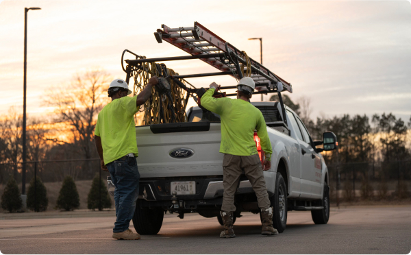 Two workers putting equipment in truck at sunset.