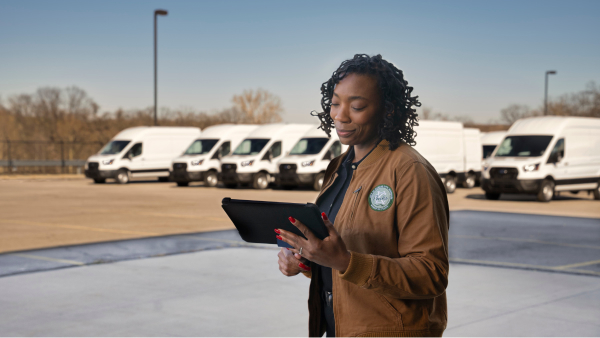 Woman holding work tablet in parking lot with Ford delivery vans